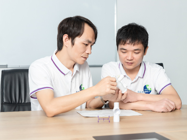 Two staff members are discussing the program, with samples and drawings of injection molded products on the table.