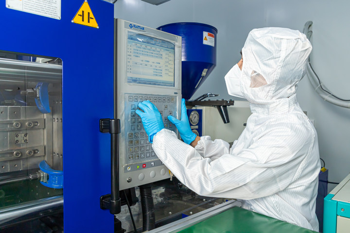 A staff member in a clean suit is operating an injection molding machine.