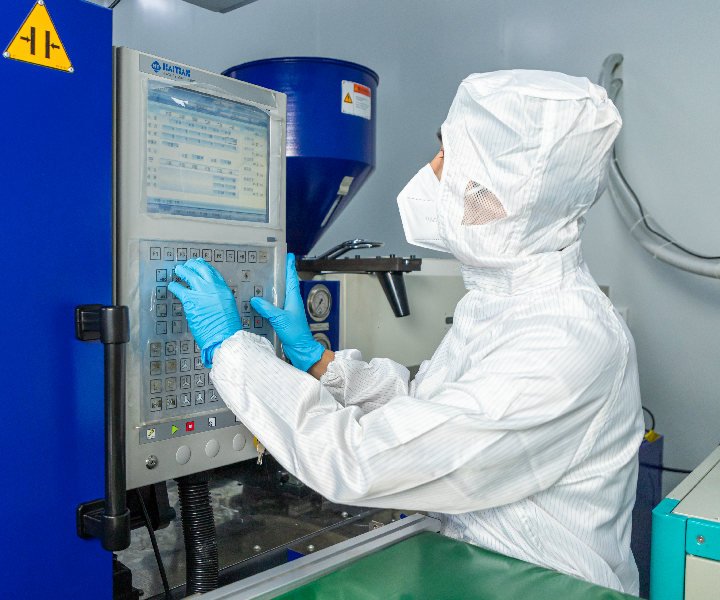 A staff member in a clean suit is operating an injection molding machine.