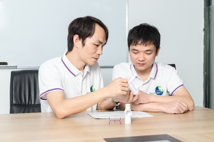 Two staff members are discussing the program, with samples and drawings of injection molded products on the table.