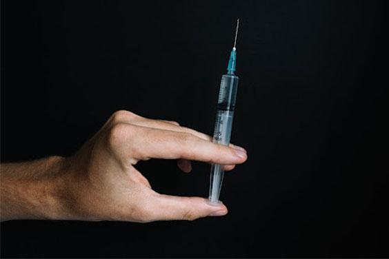 Person Holding a Syringe on Black Background