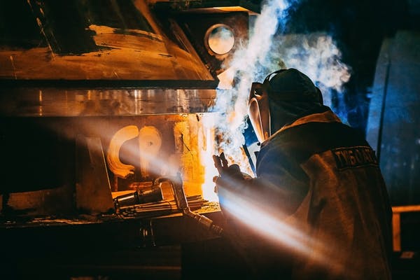 Person Wearing Gray Jacket and Welding Helmet